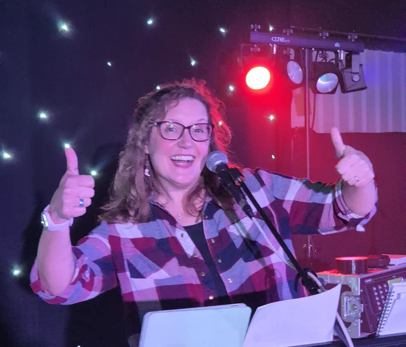 Sarah behind her keyboard rig at a band gig, giving two thumbs up