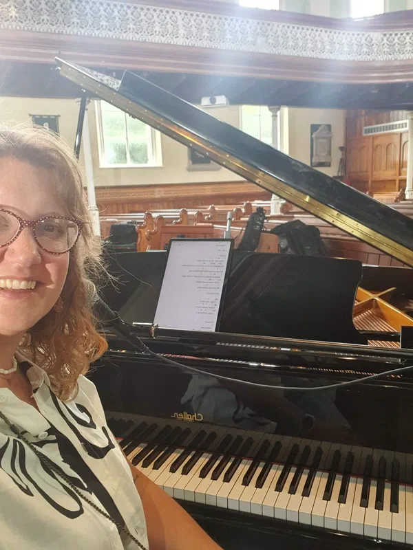 Sarah beside a grand piano in a church setting