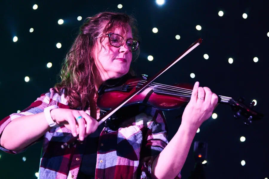 Sarah performing electric violin under stage lighting