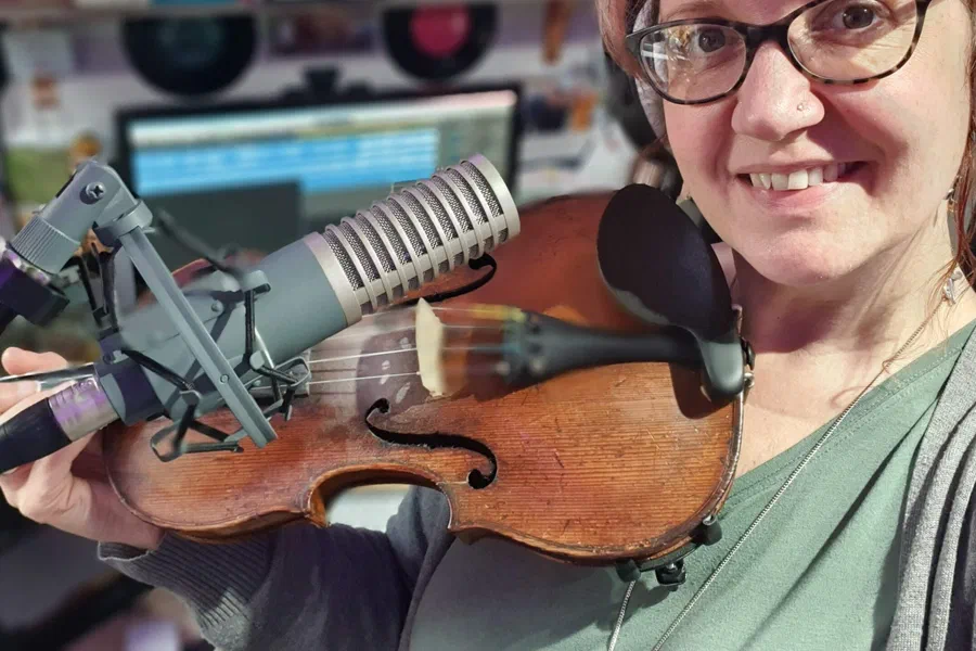 Violin beside a studio microphone with a DAW and vinyl shelf behind