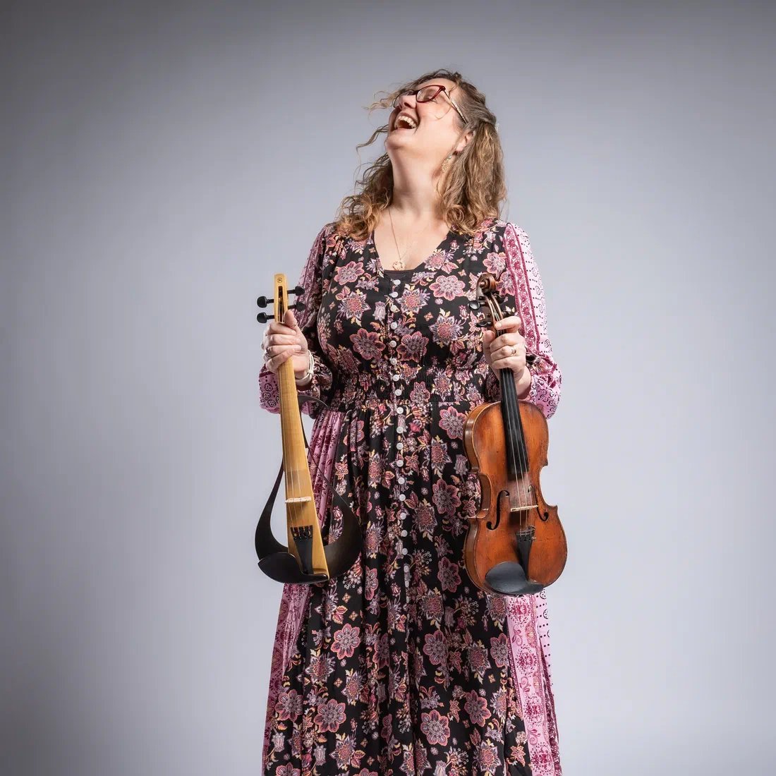 Sarah Ballard laughing, holding her violin and electric violin