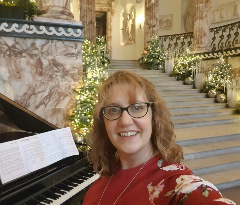 Sarah smiling beside a grand piano in front of the marble Christmas staircase at Holkham Hall